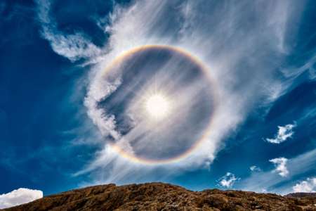 Bright sun in a rainbow circle against a blue sky with dramatic cirrus clouds